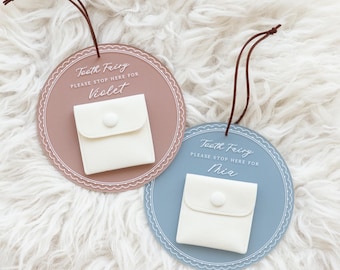 May include: Two tooth fairy boxes, one pink and one blue, with a small white pouch attached to each. The pink box says "Tooth Fairy Please Stop Here For Violet" and the blue box says "Tooth Fairy Please Stop Here For Mia".