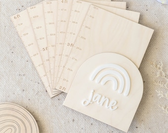May include: A wooden growth chart with a rainbow and the name "Jane" written in white. The chart has a ruler with measurements in inches and feet.