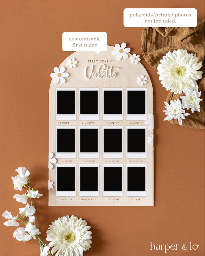 May include: A wooden photo display with a white arch shape and 12 photo slots. The display is decorated with white flowers and the text "FIRST YEAR OF Violette".