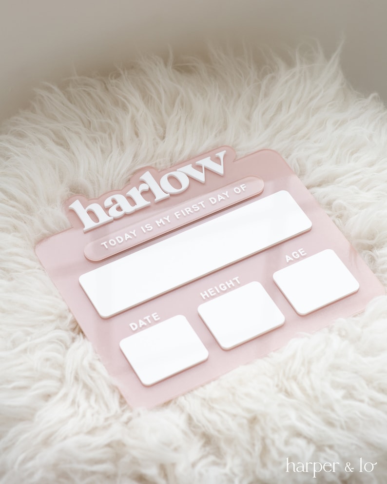 May include: Pink baby milestone tracker with the name "harlow" in white lettering. The tracker has spaces to fill in the date, height, and age.