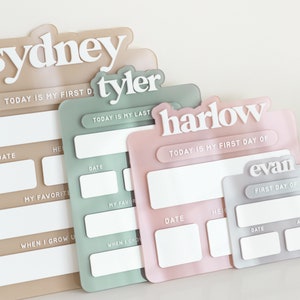May include: Four personalized acrylic signs with blank spaces for writing in. The signs are in different colors: beige, green, pink, and gray. The signs have the names Sydney, Tyler, Harlow, and Evan. The signs have the text "Today is my first day of" and "Today is my last day of".