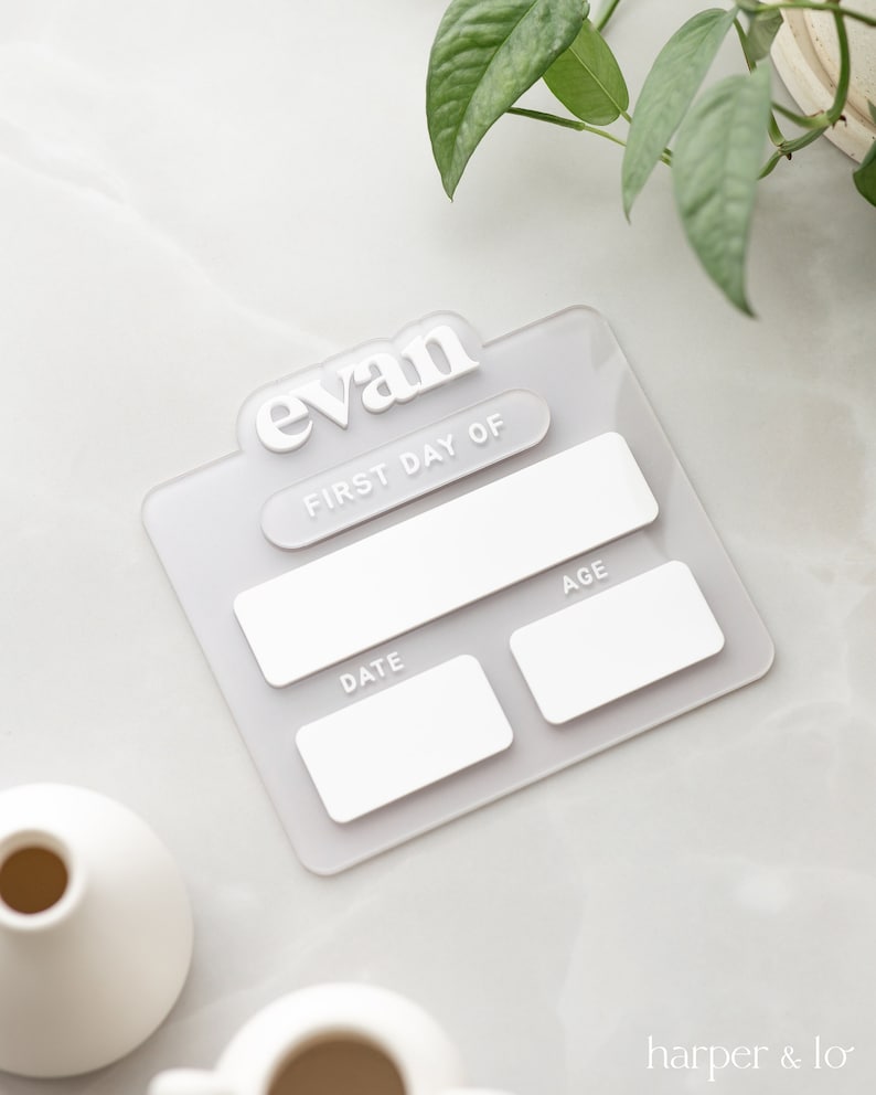 May include: White acrylic plaque with the name "Evan" in bold white letters. The plaque has a blank space for "First Day Of", a blank space for "Date", and a blank space for "Age".