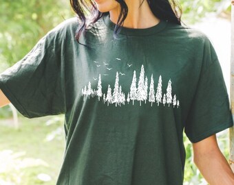 May include: A dark green t-shirt featuring a white graphic of a forest silhouette. The graphic includes trees and birds.