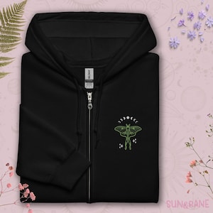 May include: Black zip-up hoodie with a green embroidered moth and moon phases design. The text "SUN & RANE" is visible in the bottom right corner.