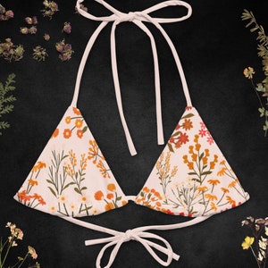May include: A white bikini top with a floral print featuring orange, yellow, and red flowers. The top has adjustable straps and a tie closure at the back.