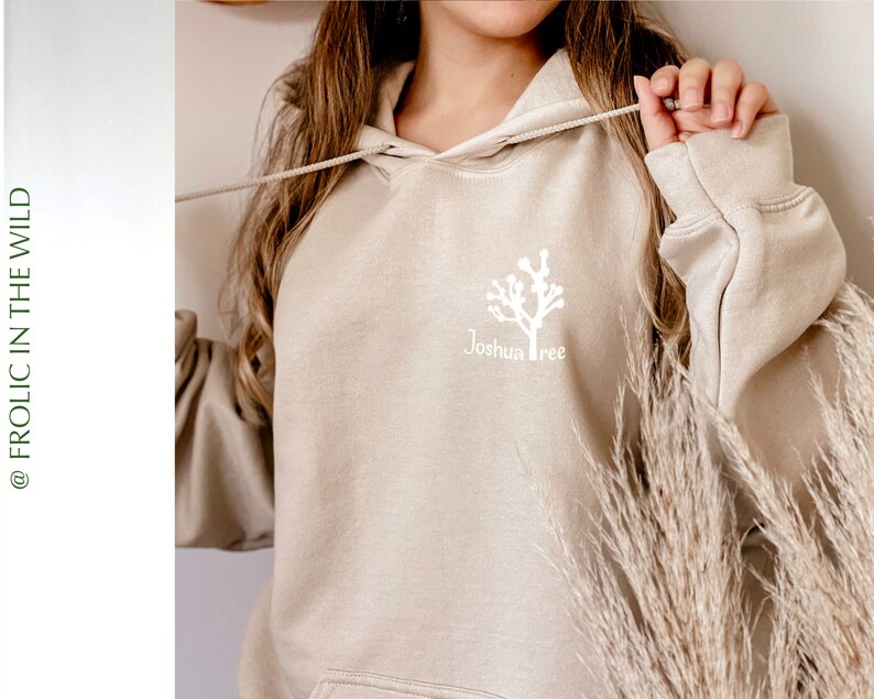May include: A beige hoodie with a white Joshua Tree graphic on the front. The hoodie has a drawstring hood and a kangaroo pocket.