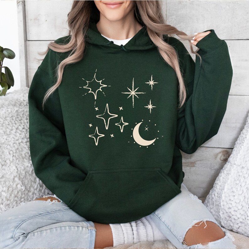 May include: A dark green hooded sweatshirt with a cream-coloured design of stars and a crescent moon.