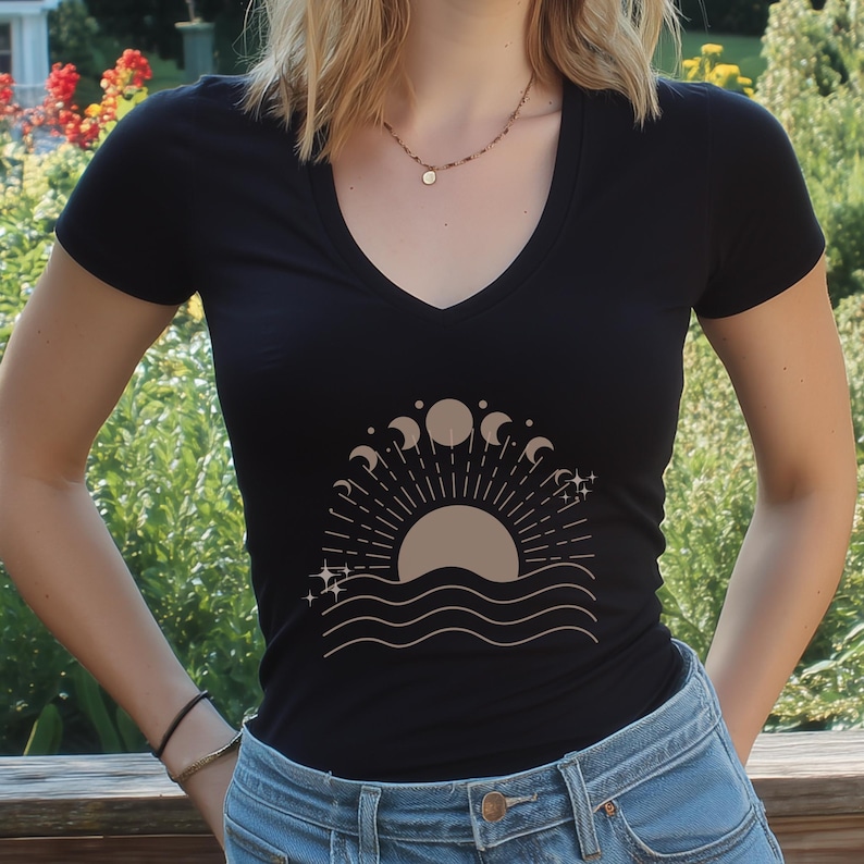 May include: Black V-neck t-shirt featuring a beige graphic of a sun, moon phases, and waves. The design includes radiating lines and stars. The shirt is made of a soft material.