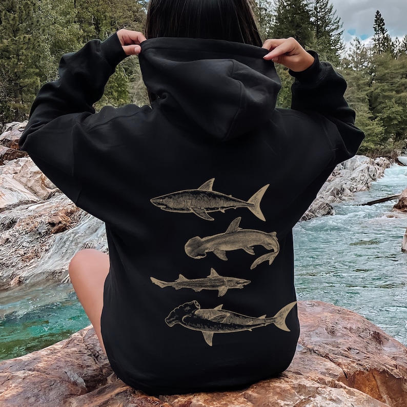 May include: Black hoodie with a graphic print of four different types of sharks on the back. The sharks are in a vintage style and are all facing the same direction.