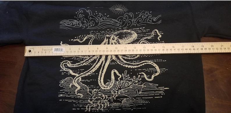 May include: Black t-shirt with a white graphic of an octopus with tentacles and waves. The octopus is surrounded by a white border.
