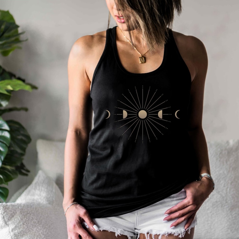 May include: Black tank top with a celestial design featuring a sunburst, moon phases, and a central sun. The graphic is in a gold color. The top has a racerback style.