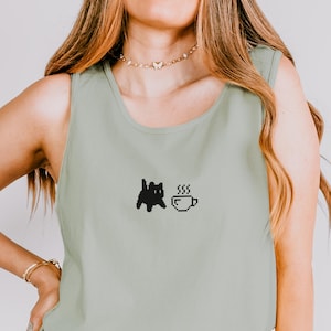 Op de afbeelding: Saliegroen tanktop met een zwart gepixeld kat- en koffiekopje-ontwerp. De mouwloze top is gemaakt van een zacht materiaal en is geschikt voor vrijetijdskleding. Het kat- en koffiekopje-ontwerp is een schattige en eenvoudige afbeelding.