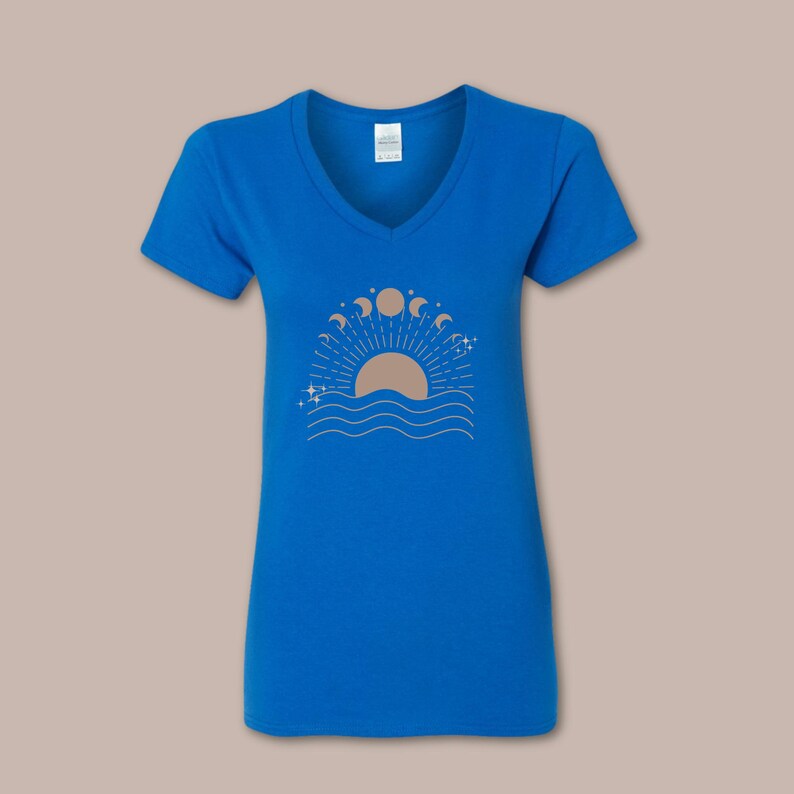 May include: A royal blue V-neck t-shirt featuring a beige graphic of a sun setting over wavy lines, with phases of the moon and stars. The design is centered on the front of the shirt.