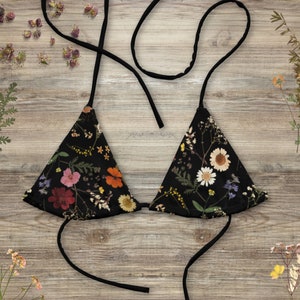 May include: A black bikini top with a floral print featuring dried flowers. The top has adjustable straps and a triangle shape.