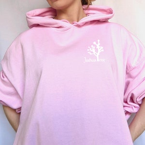 May include: A pink oversized hoodie with a white graphic of a Joshua Tree and the text "Joshua Tree" on the front.