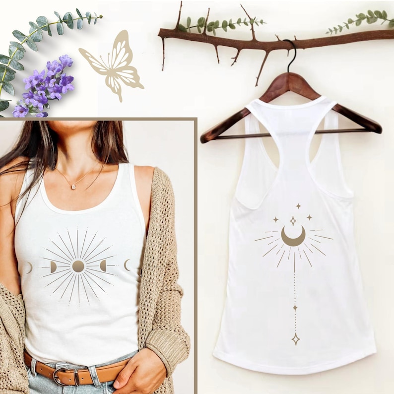 May include: White tank top with a celestial sun and moon design on the front. The back of the tank top features a crescent moon, stars, and a line of dots and diamonds. The tank top is hanging on a wooden hanger.