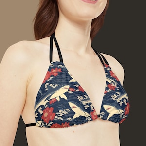 Op de afbeelding: Een zwarte bikini top met verstelbare bandjes met een blauwe en witte print van haaien en rode bloemen.