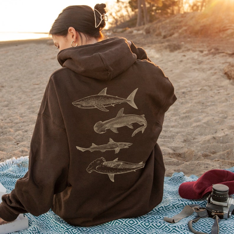 May include: A brown hoodie with a graphic print of four different types of sharks on the back. The sharks are all in a light brown color and are facing different directions.
