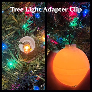 May include: A white plastic adapter clip for Christmas tree lights. The clip is attached to a string of lights and is holding a round, orange light bulb. The light bulb is glowing.