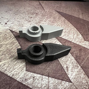 May include: Two 3D printed plastic pieces in the shape of a pointed arrow. One piece is grey and the other is black.