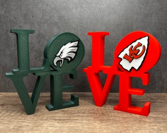 May include: Green and red wooden "LOVE" sign with the Philadelphia Eagles and Kansas City Chiefs logos.