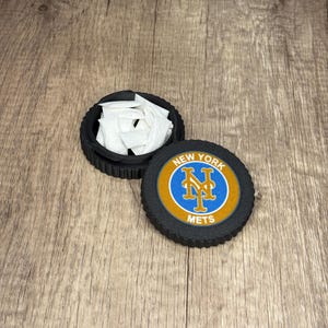 May include: A black and blue round container with the words "New York Mets" on it. The container is open and filled with white triangular pieces of paper.