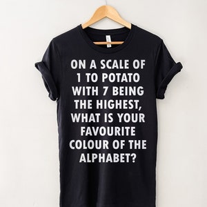 May include: Black t-shirt with white text that reads "On a scale of 1 to potato with 7 being the highest, what is your favourite colour of the alphabet?"