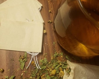 May include: A close-up of a glass of tea with loose leaf tea in a muslin tea bag. The tea bag is on a wooden surface with loose leaf tea scattered around it.