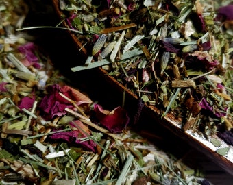 May include: Close-up of a wooden scoop filled with a blend of dried herbs and flowers. The mix includes green leaves, lavender buds, and deep red rose petals. The wooden scoop is partially visible, casting a shadow on the surface.