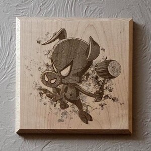 May include: A wooden plaque featuring a cartoon illustration of Spider-Man holding a mallet. The artwork is etched in shades of gray and black, with a splash effect in the background. The plaque has a natural wood grain finish.