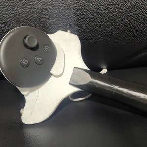 Puede incluir: Un dispositivo blanco impreso en 3D con un controlador circular negro adjunto. El controlador tiene botones etiquetados como 'A' y 'B' y una palanca de mando redonda. El dispositivo tiene un mango negro.