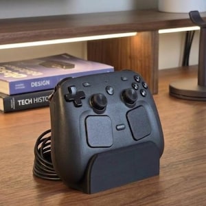 May include: A black wired video game controller featuring a directional pad, two analog sticks, four action buttons, and two large touch-sensitive panels on the front, resting upright in a matching black plastic stand with a coiled black cable.