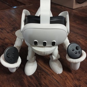 Könnte beinhalten: Weißer Plastikständer mit einem weißen VR-Headset und zwei schwarzen Controllern. Der Ständer ist so konzipiert, dass er das VR-Headset und die Controller an Ort und Stelle hält.