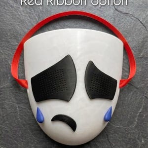May include: A white mask with black eye coverings, a black curved mouth, and blue teardrops. A red ribbon is attached to the top of the mask. The text "Red Ribbon option" is at the top of the image.