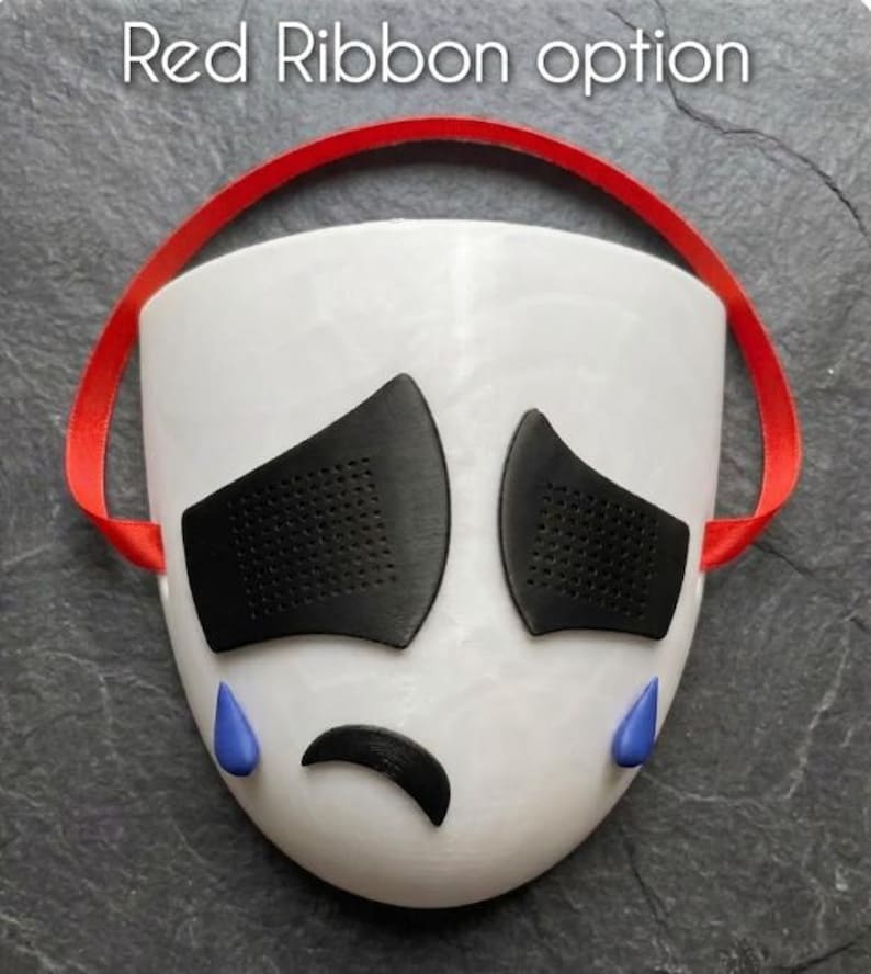 May include: A white mask with black eye coverings, a black curved mouth, and blue teardrops. A red ribbon is attached to the top of the mask. The text "Red Ribbon option" is at the top of the image.