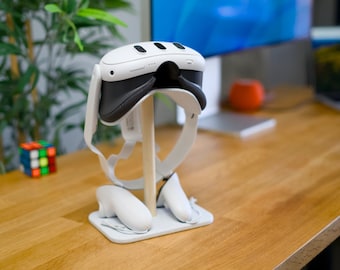 May include: A white virtual reality headset with black accents is displayed on a stand with two white controllers. The headset is on a wooden surface.
