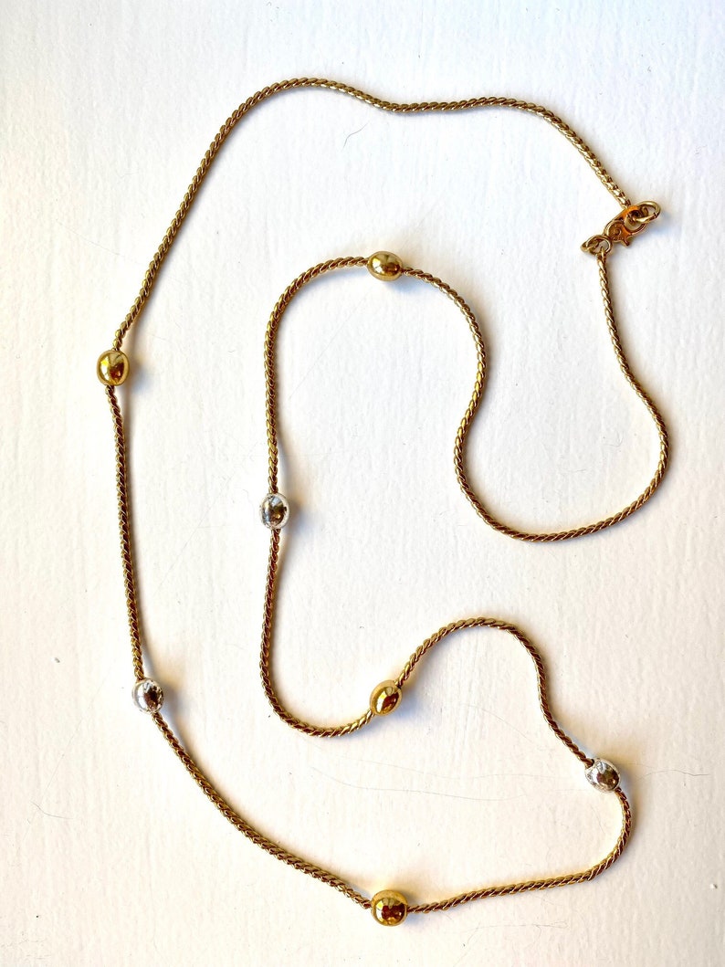 May include: A gold chain necklace with alternating gold and silver round beads. The chain is a twisted rope design.