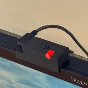 Może przedstawiać: Czarna osłona kamery internetowej z czerwoną lampką kontrolną jest przymocowana do górnej części monitora. Osłona kamery internetowej jest podłączona do czarnego kabla z nazwą marki "ANKER" wydrukowaną na złączu.