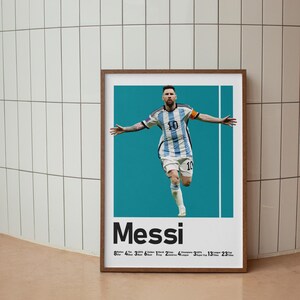 May include: Framed poster featuring Lionel Messi in an Argentina soccer uniform, arms outstretched. The poster has a teal background with the name "Messi" in bold letters. Below the name are numbers and titles.