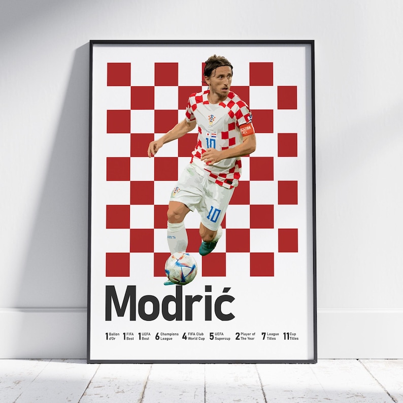 Puede incluir: Un p&oacute;ster enmarcado que muestra a un futbolista con camiseta de cuadros rojos y blancos y pantalones cortos blancos, regateando un bal&oacute;n. El fondo tiene un patr&oacute;n de cuadros rojos y blancos. El texto dice Modrić, seguido de sus logros.