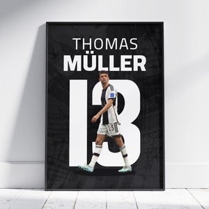 Op de afbeelding: Een zwart-witte poster met de naam "Thomas Müller" en het nummer "13" in groot wit lettertype. Een voetballer in een wit shirt met nummer "13" loopt op de poster.