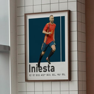 K&ouml;nnte beinhalten: Ein gerahmtes Poster mit einem Fu&szlig;ballspieler in einem rot-schwarzen Trikot, unter dem der Name "Iniesta" steht. Der Spieler rennt mit dem Ball und hat einen entschlossenen Gesichtsausdruck.