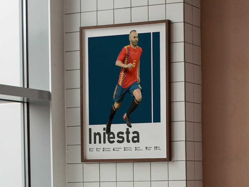 K&ouml;nnte beinhalten: Ein gerahmtes Poster mit einem Fu&szlig;ballspieler in einem rot-schwarzen Trikot, unter dem der Name "Iniesta" steht. Der Spieler rennt mit dem Ball und hat einen entschlossenen Gesichtsausdruck.
