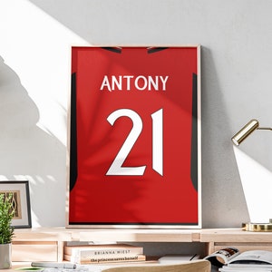 以下が含まれることがあります： 名前が「ANTONY」で番号が「21」の赤と黒のサッカーユニフォームです。