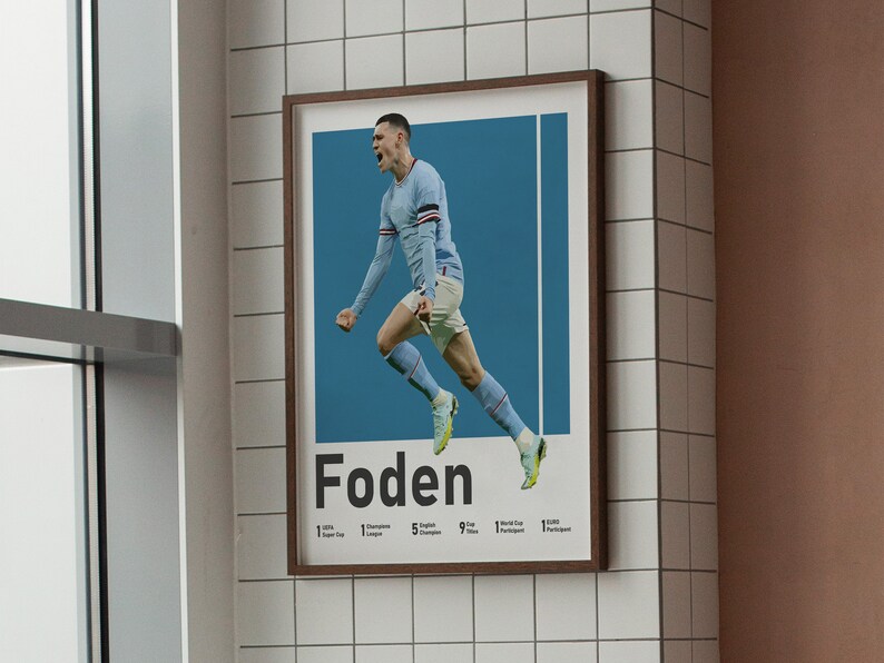 May include: A poster featuring a football player in a blue shirt celebrating a goal. The player is in mid-air with his arms raised. The poster has the player's name "Foden" in large black letters at the bottom. The poster also lists the player's achievements, including 1 Premier League title, 1 Champions League title, 5 English Super Cup titles, 9 Premier League Player of the Month awards, 1 World Cup participant, and 1 Euro participant.