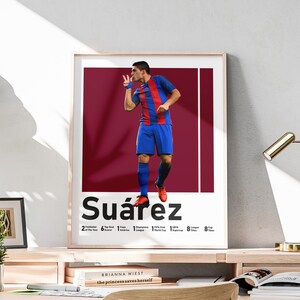 Może przedstawiać: A framed poster featuring a soccer player in a blue and red uniform, making a gesture. The poster displays the name "Su&aacute;rez" and statistics. The background is a deep red. The poster is in a light-colored wooden frame.
