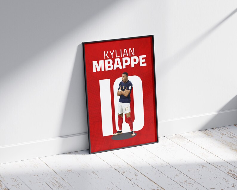 以下が含まれることがあります： 赤い背景に白い文字で「Kylian Mbappe 10」と書かれた額縁付きポスター。ポスターの中央には、青いユニフォームを着て背番号10のサッカー選手の画像が写っている。