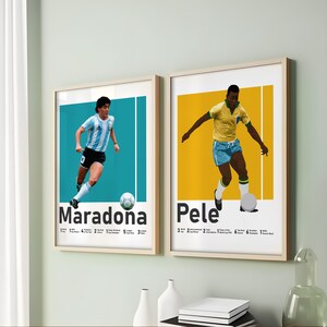 May include: Two framed art prints showcasing football legends Maradona and Pele. Maradona is in an Argentinian strip, and Pele in a Brazilian strip. Each print has a coloured background and includes the player's name and achievements.