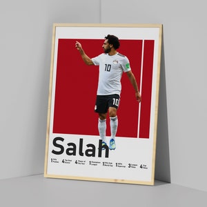 K&ouml;nnte beinhalten: Ein Poster mit einem Foto von Mohamed Salah, einem &auml;gyptischen Profi-Fu&szlig;baller, der ein wei&szlig;es Trikot mit der Nummer 10 tr&auml;gt. Das Poster hat einen roten Hintergrund und den Text "Salah" in Schwarz. Das Poster enth&auml;lt auch eine Liste von Salahs Leistungen, darunter "FIFA Puskas Award", "Top-Torsch&uuml;tze", "Spieler des Jahres", "Champions League", "FIFA Club World Cup", "UEFA Super Cup", "Liga-Titel" und "Pokal-Titel".