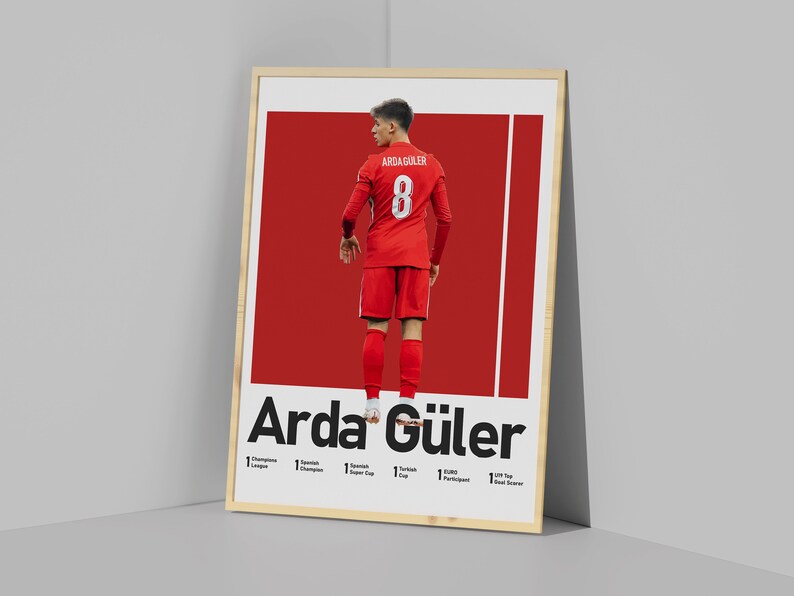 May include: A poster featuring a soccer player in a red jersey with the number 8 on the back. The player is standing with their back to the camera. The poster has the text "Arda G&uuml;ler" in bold black letters at the bottom. The poster also lists the player's accomplishments, including "1 Turkish Cup", "1 UEFA Participant", and "1 Top Scorer".